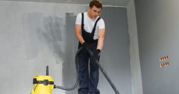 male worker in overall vacuum cleaning during apartment renovation.