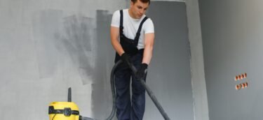 male worker in overall vacuum cleaning during apartment renovation.