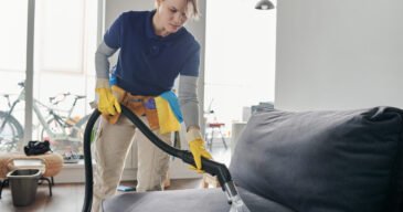 Professional cleaning service worker vacuuming the sofa with vacuum cleaner in the living room