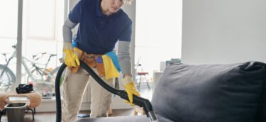 Professional cleaning service worker vacuuming the sofa with vacuum cleaner in the living room