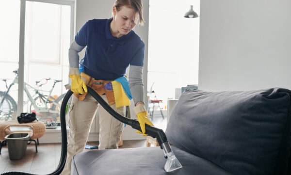 Professional cleaning service worker vacuuming the sofa with vacuum cleaner in the living room