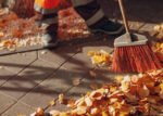 Janitor cleaner sweeping autumn leaves on the street