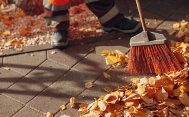 Janitor cleaner sweeping autumn leaves on the street