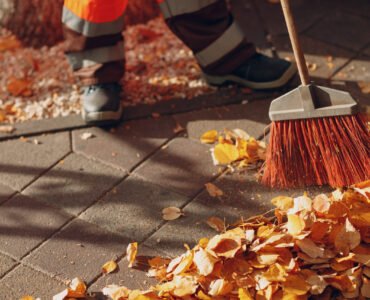 Janitor cleaner sweeping autumn leaves on the street