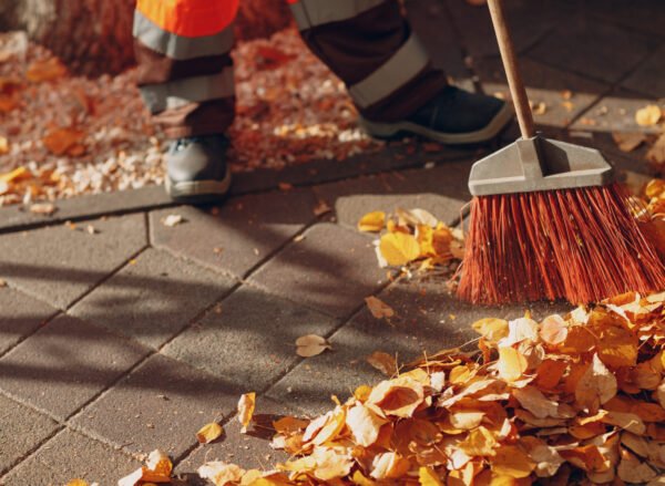 Janitor cleaner sweeping autumn leaves on the street